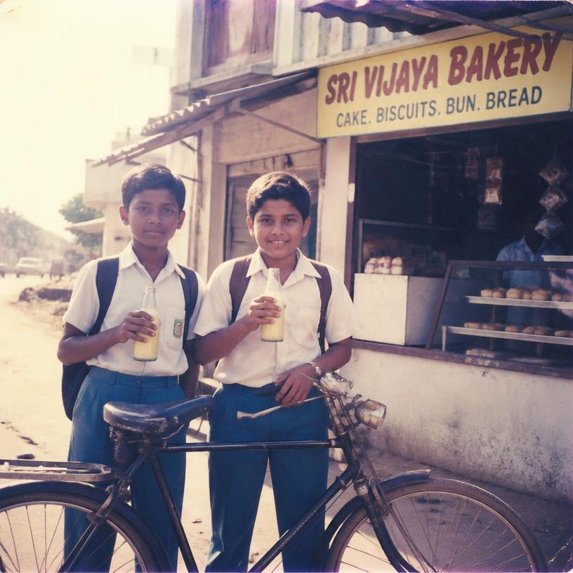 Two schoolboys with a bicycle holding milk bottles outside a bakery, 1990s