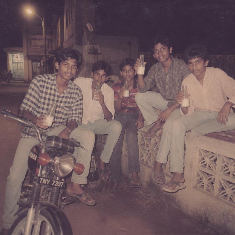 Friends sitting on a bike and a wall at night with milk bottles