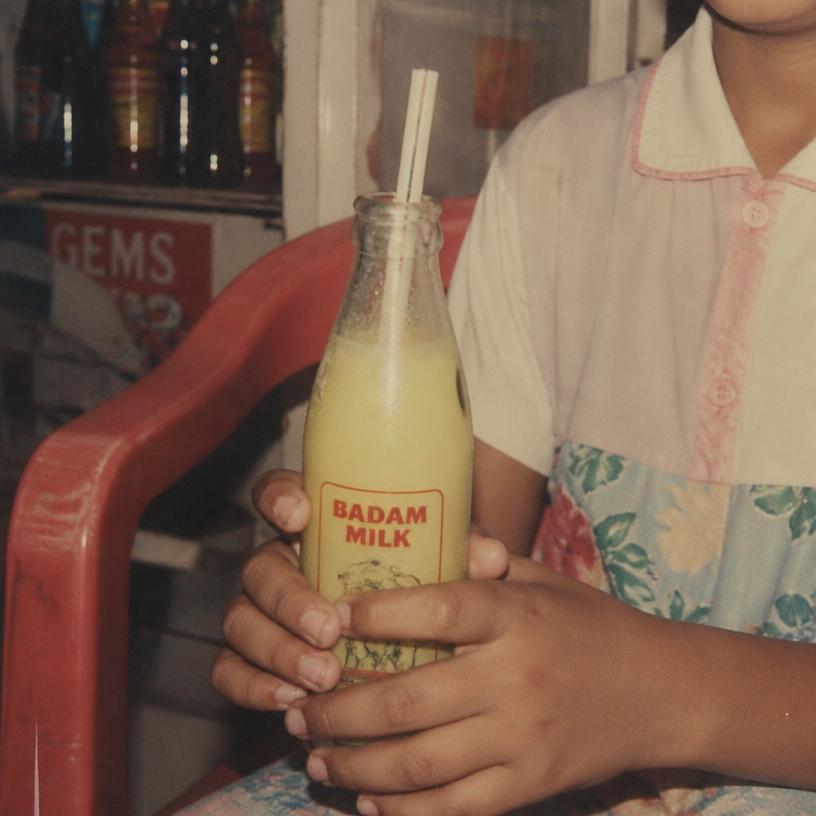 A child holding a cold bottle of badam milk with a straw
